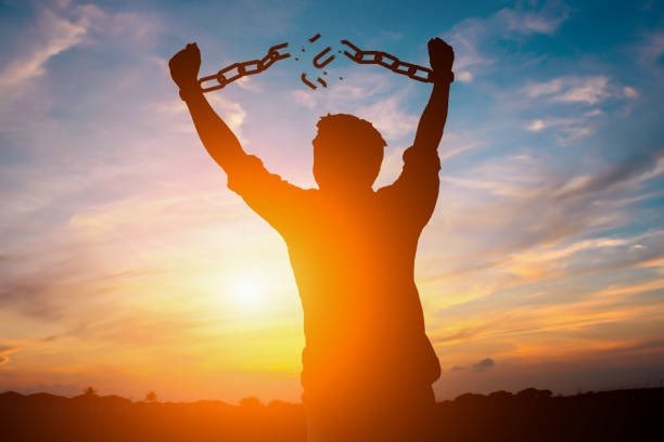 Persona en contra luz del sol liberándose de sus cadenas